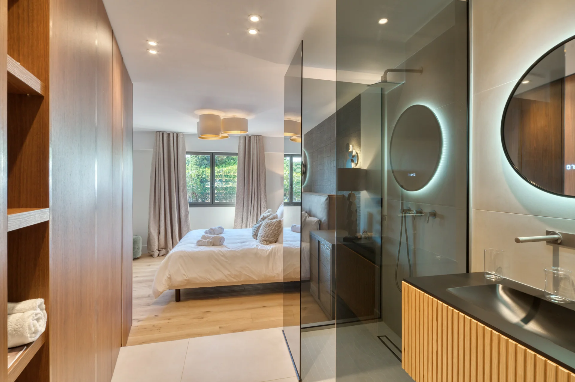 Salle d’eau ouverte sur la chambre, douche vitrée et miroir rond