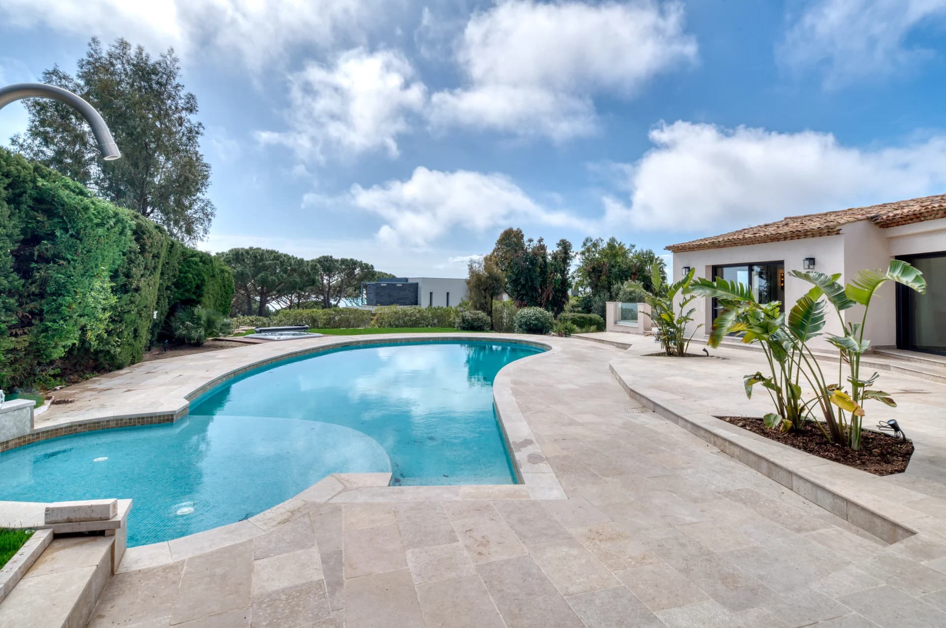 La piscine en forme libre, terrasse en travertin et massifs de strelitzias