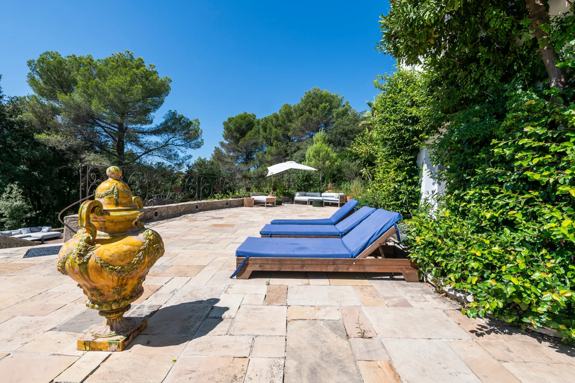 Terrasse de pierre, bains de soleil bleus et vasque en faïence jaune