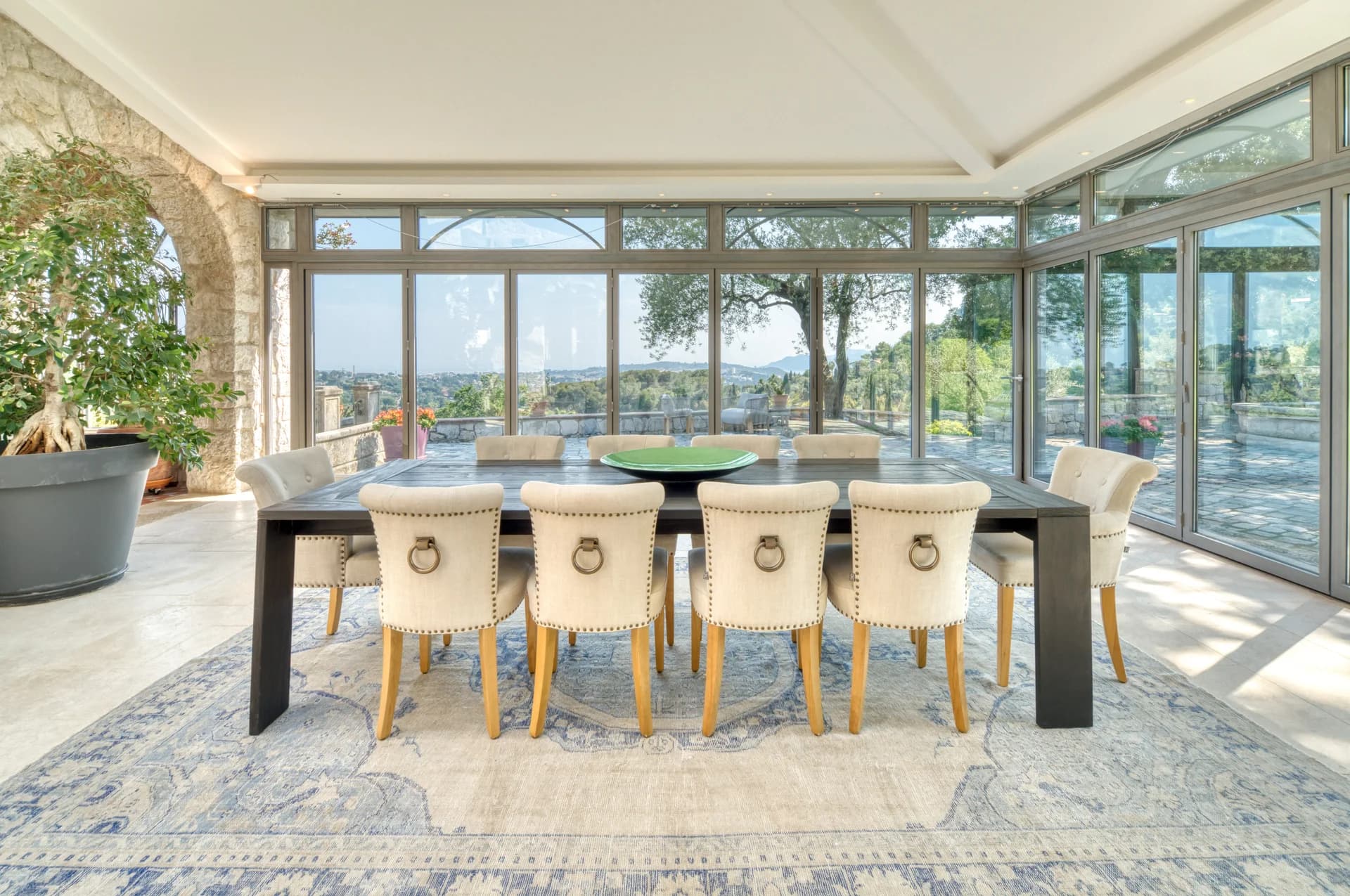 Salle à manger vitrée, table en bois et vue sur les collines