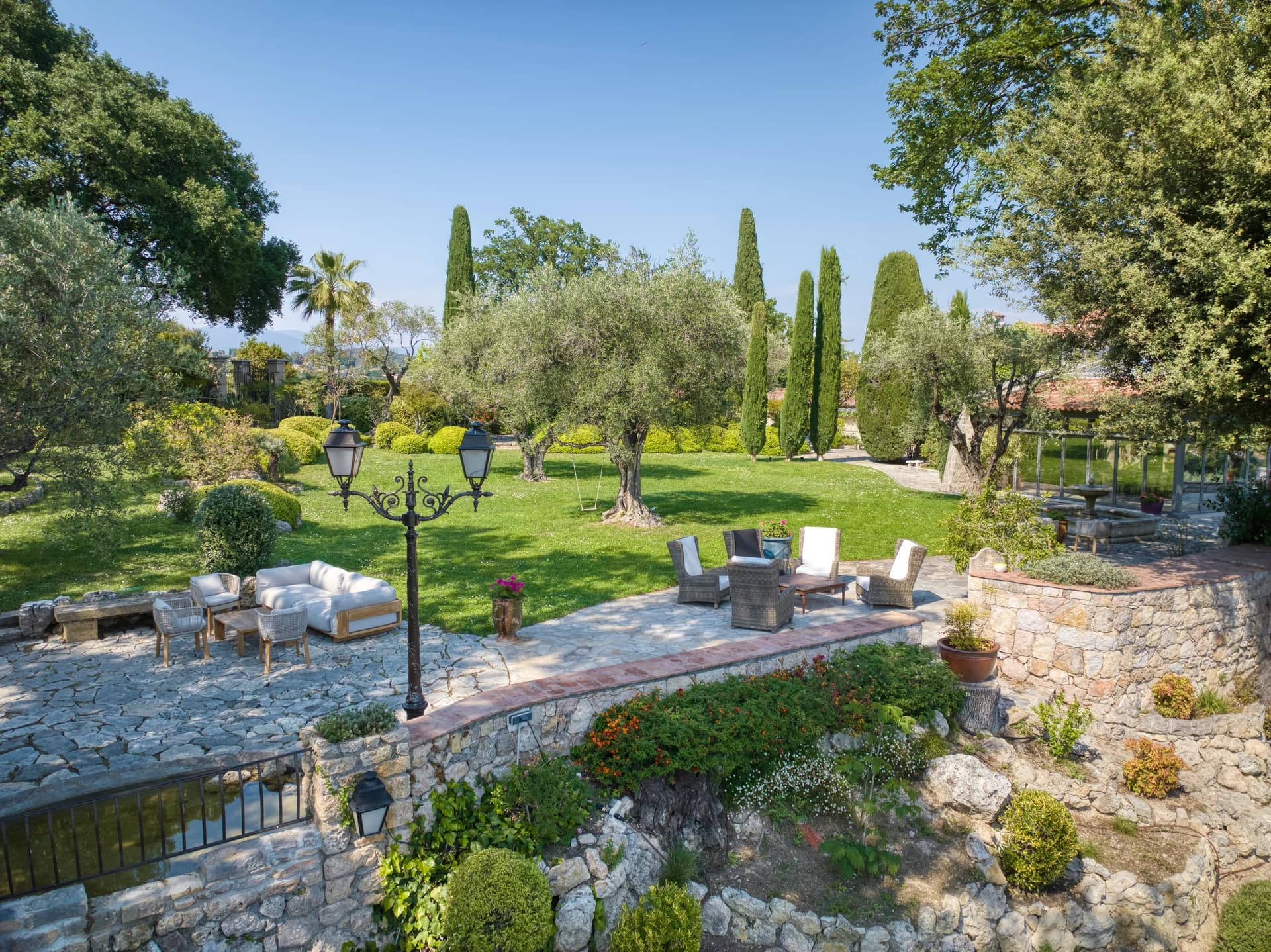 Terrasse dallée et salon de jardin, oliviers et cyprès sur la pelouse